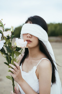 年轻的亚洲长发黑发女子新娘的肖像，戴着白色面纱，在户外捧着白玫瑰。