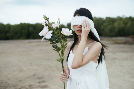 年轻的亚洲长发黑发女子新娘的肖像，戴着白色面纱，在户外捧着白玫瑰。