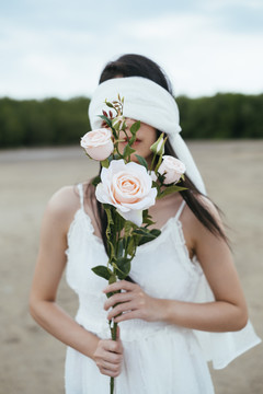 年轻的亚洲长发黑发女子新娘的肖像，戴着白色面纱，在户外捧着白玫瑰。