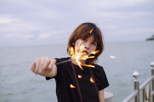 年轻的亚洲短发女子在沙滩上拿着火花弹玩耍的肖像。