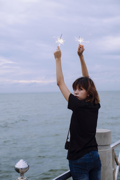 背景图：年轻的泰国亚裔女子短发举手举着两个火花头在海滩上在杜什时间。回头看摄像机。