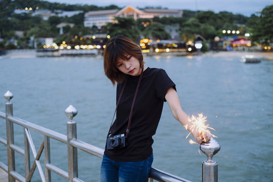 黄昏时分，一位年轻的泰国亚裔女摄影师在沙滩上玩着火花。