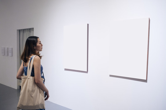 美丽的亚洲年轻女子在美术馆里看着空白的纸画布。