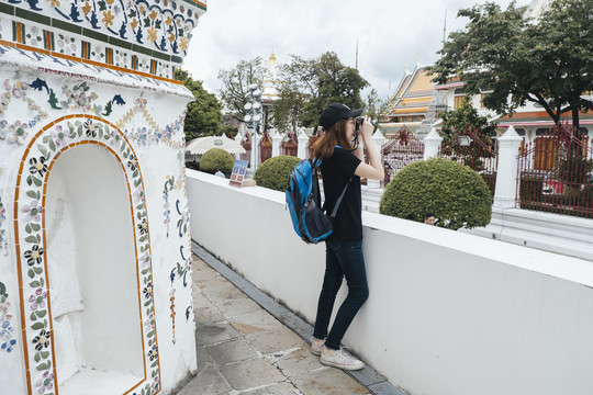 亚洲背包客妇女在wat arun用相机拍照的侧视图。