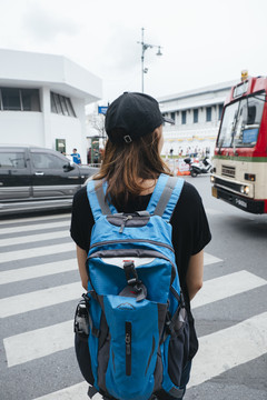 穿黑色衬衫的背包客妇女在曼谷横穿马路的后视图。