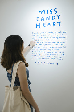 在美术馆的墙上，一位穿着蓝色裙子的亚洲时髦美女正在阅读文字。