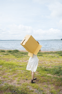 年轻的亚泰女性嬉皮士卷发白色连衣裙覆盖上半身纸箱走进湖中。