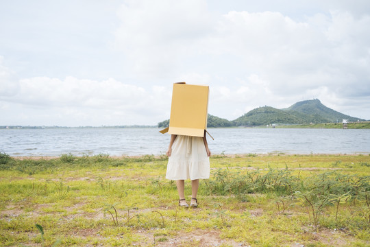 年轻的泰国亚裔女子嬉皮卷发在白色连衣裙覆盖纸板箱上身在湖。