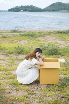 年轻的泰国亚裔女子时髦卷发白色连衣裙坐在户外打开纸板箱。