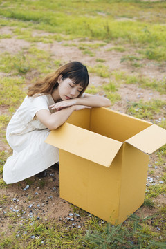 年轻的泰国亚裔女子时髦卷发白色连衣裙坐在户外打开纸板箱。