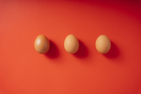 红色背景上分离出三个棕色的鸡蛋。