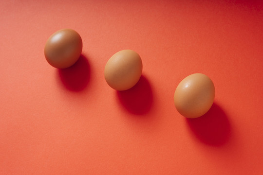 红色背景上分离出三个棕色的鸡蛋。