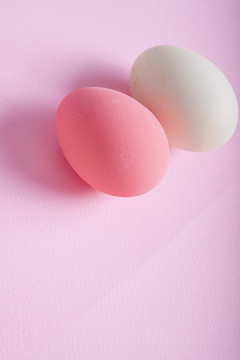 粉红色背景上的粉红色鸡蛋和白色鸡蛋。垂直射击。