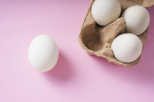 顶视图-白色鸡蛋和粉红色背景上的盒子。