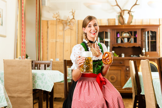 年轻女子在传统的巴伐利亚州餐厅或酒吧里喝啤酒、牛排和椒盐卷饼