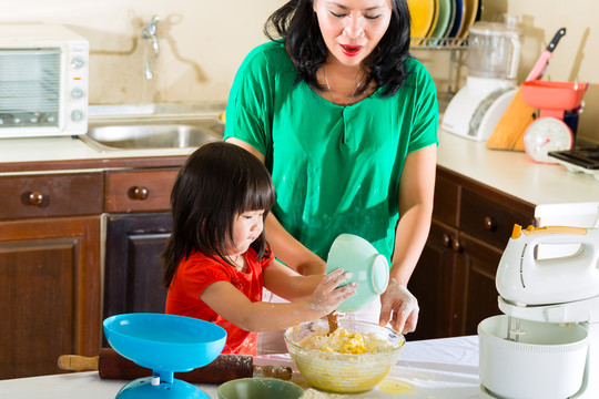 印尼亚裔小女孩和妈妈在厨房一起烤蛋糕