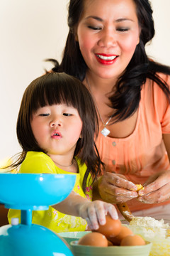 印尼亚裔小女孩和妈妈在厨房一起烤蛋糕