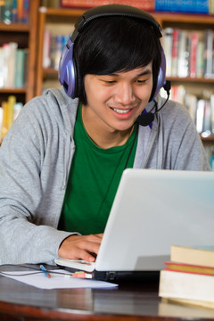 学生-亚洲年轻人在图书馆用手提电脑和耳机学习