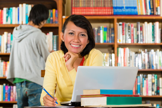 学生——图书馆里拿着笔记本电脑学习的年轻女子，一名男学生站在书架上看书