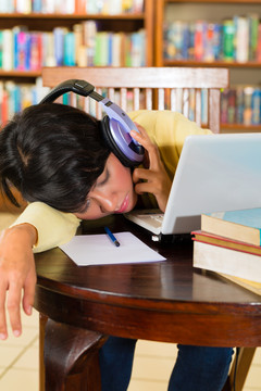 学生-年轻女子在图书馆用笔记本电脑学习，她筋疲力尽，睡着了