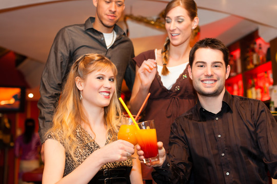 年轻幸福的夫妇在酒吧或餐厅喝鸡尾酒，朋友们站在后台
