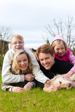 一家人，父亲，母亲和女儿，和他们的狗一起坐在草地上，他们欢笑着，玩得很开心