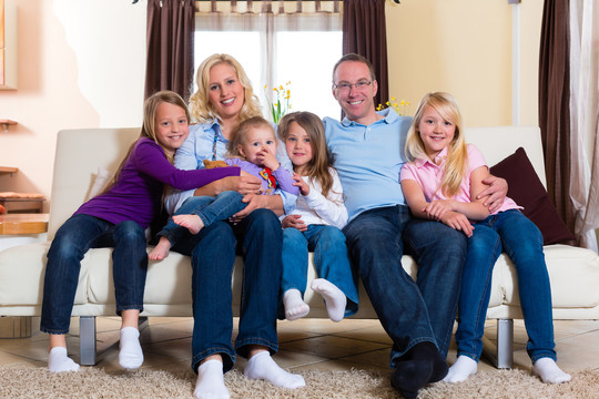一家人，父亲，母亲和四个姐妹坐在客厅的沙发上