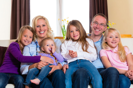 一家人，父亲，母亲和四个姐妹坐在客厅的沙发上