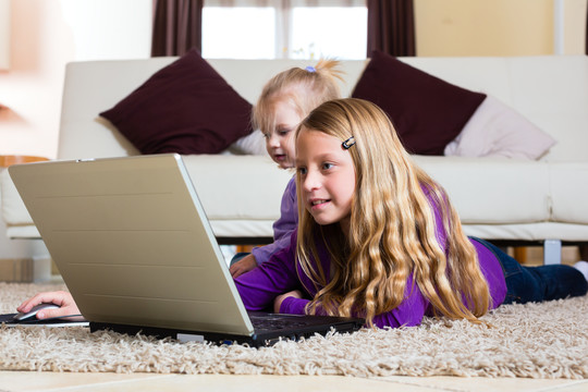 家里的孩子在地板上玩笔记本电脑，她的小妹妹和她在一起