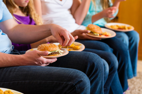年轻的家庭——母亲、父亲和女儿——正在家里吃汉堡包或快餐
