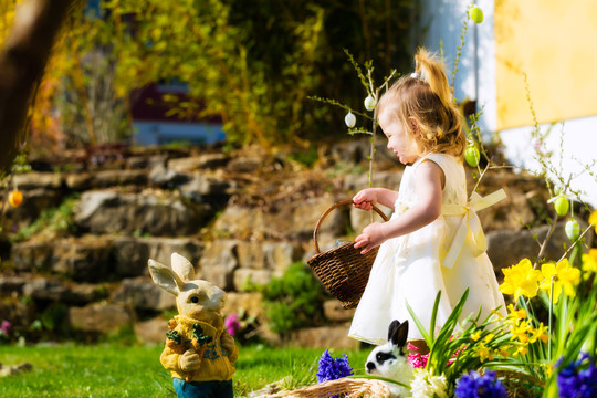 春天，小女孩在草地上寻找复活节彩蛋，她手里拿着一个篮子或复活节篮子