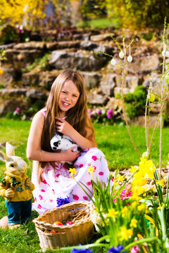 春天，小女孩在草地上寻找复活节彩蛋，她抱着一只活兔子