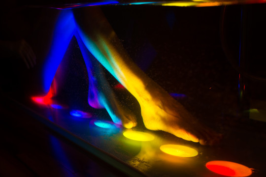 在水疗中心用色彩疗法洗澡的女士，浴缸用五颜六色的灯光照明（聚焦前景中的泡泡）