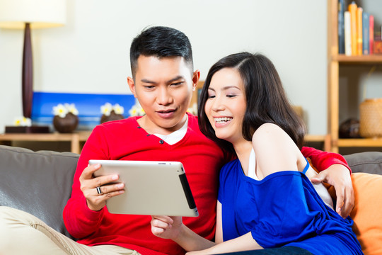 一对年轻的印尼夫妇——一男一女——坐在沙发上，手里拿着一台平板电脑