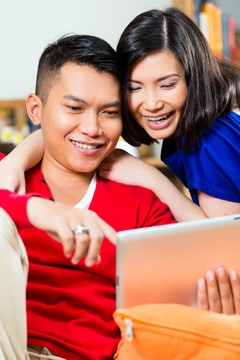 一对年轻的印尼夫妇——一男一女——坐在沙发上，手里拿着一台平板电脑
