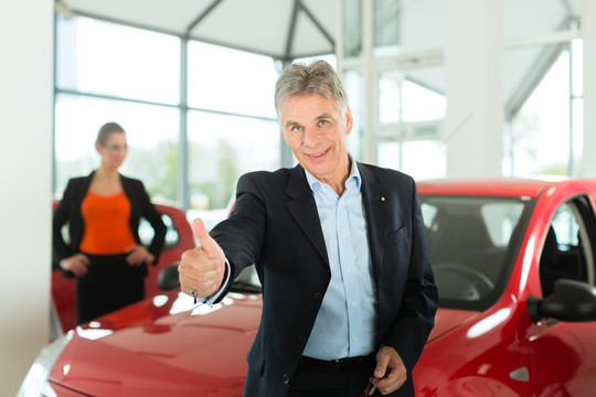 成熟的单身男子与红色汽车在轻型汽车经销商处有一位女性客户，一位年轻女子，他显然是买车或是汽车经销商