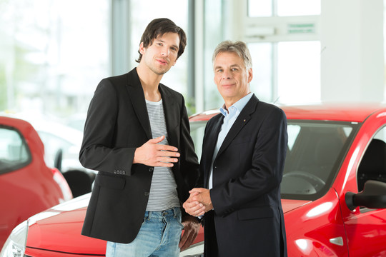 成熟的单身男子与红色汽车在轻型汽车经销商与一名男性客户，一个年轻人，他显然是买车或是一个汽车经销商