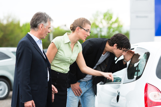 成熟的汽车经销商和年轻夫妇站在经销商的停车位前的汽车