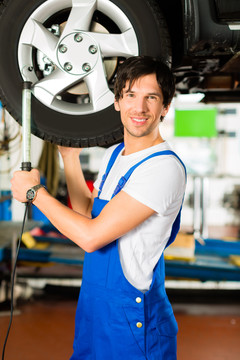 一个穿着蓝色衣服的年轻人——机修工——在一个服务站里用顶棚上的灯工作