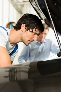 成熟的男人-客户-和年轻的机械师正在看一个带灯的引擎盖下面