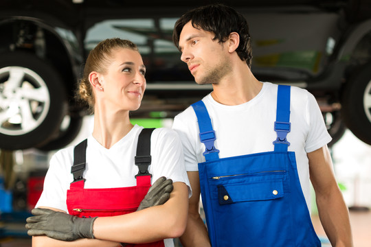 一对身穿蓝色衣服的年轻男女——机修工——站在一辆被顶起的汽车前