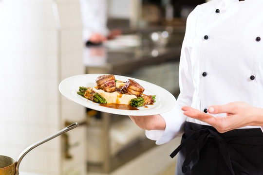 女厨师在酒店或餐厅的厨房里做饭，只有双手被人看见，她正在呈现一道菜
