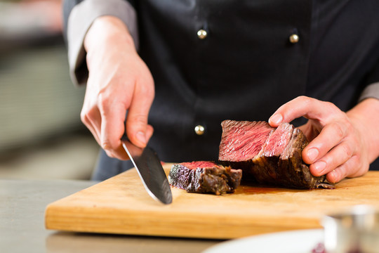 厨师在酒店或餐厅的厨房里做饭，只有双手，他正在切肉或牛排