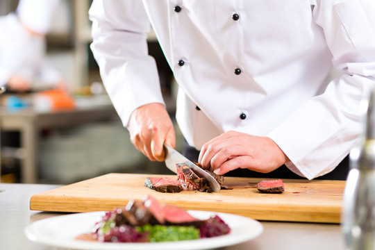厨师在饭店或餐厅的厨房里做饭，只有双手，他正在切肉或牛排，为盘子上的一道菜