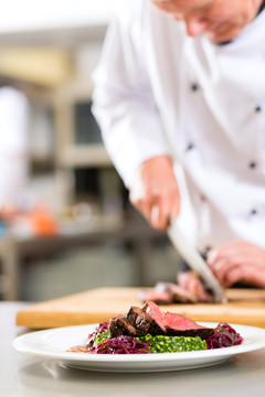 厨师在饭店或餐厅的厨房里做饭，他正在为盘子上的一道菜切肉或牛排