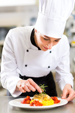 女厨师在酒店或餐厅的厨房里做饭，她正在完成盘子上的一道菜