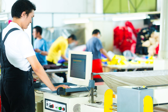 亚洲一家纺织厂的工人或生产经理在一台大机器的屏幕前工作