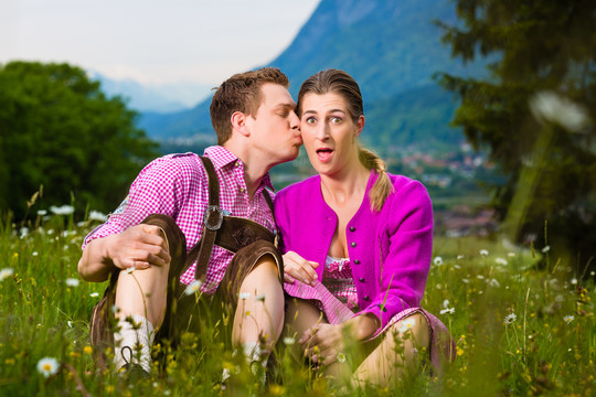 一对身着传统服饰的幸福夫妇坐在草地上欣赏着山景