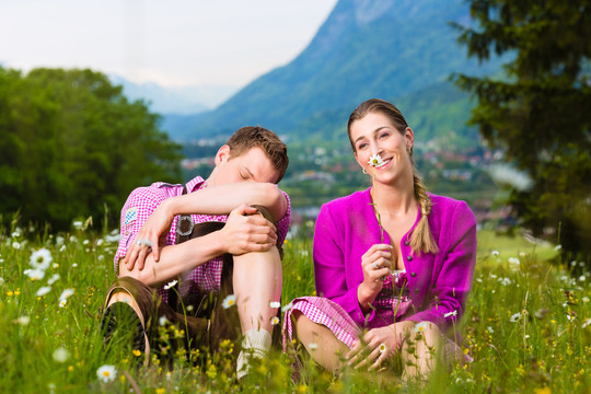 一对穿着传统服装的夫妇坐在草地上，山上的全景有一些问题