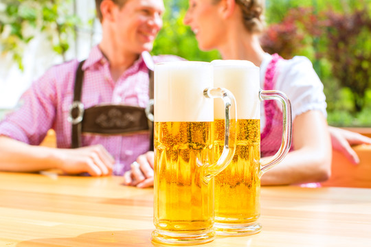 一对幸福的情侣坐在夏日的啤酒花园里，享受着一杯啤酒和阳光，在伏尔格伦站着两杯